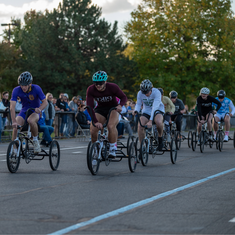 A group of participants race on tricycles in the Trike Derby at Indiana State University, with spectators watching from the sidelines.